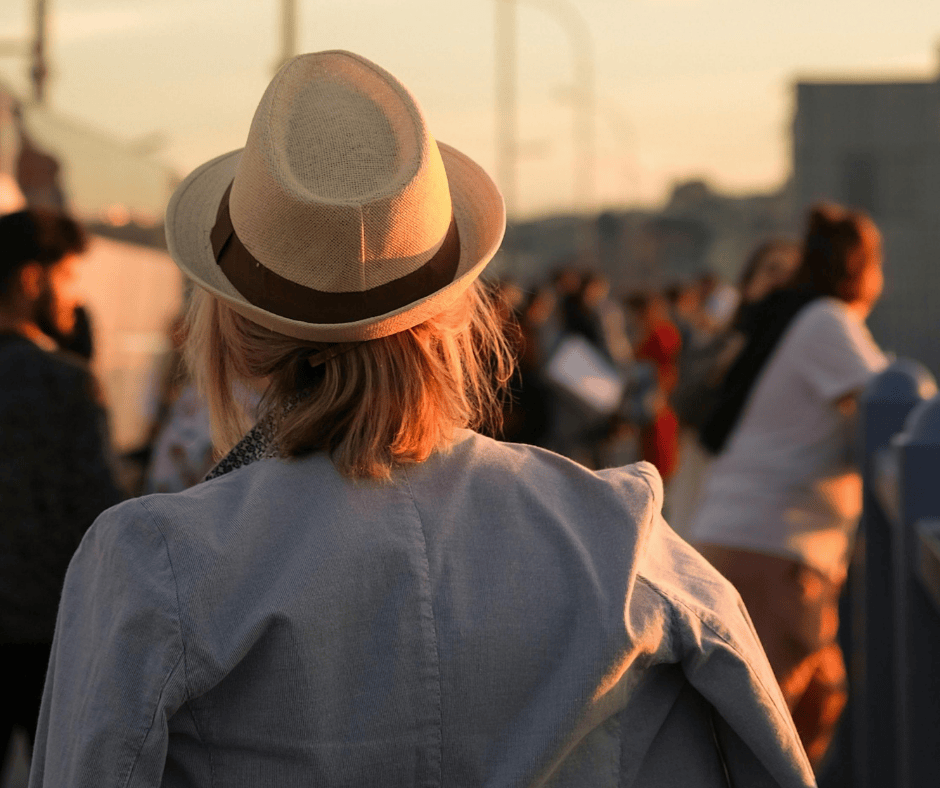 Person wearing a beige fedora hat at sunset, blending classic style with a modern urban setting.